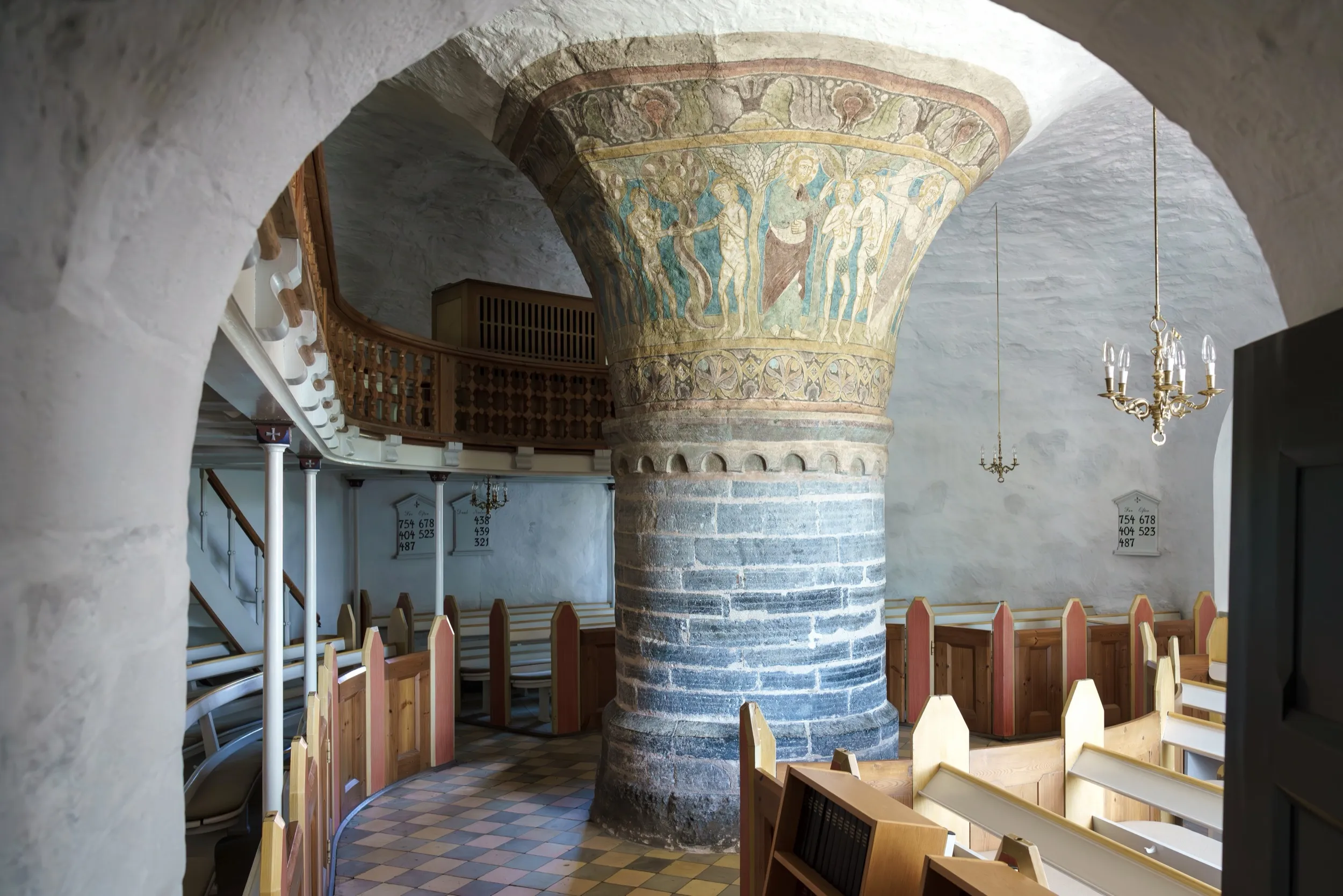 Innenraum der Nylars Kirke mit Zentralpfeiler und bunten Holzbänken