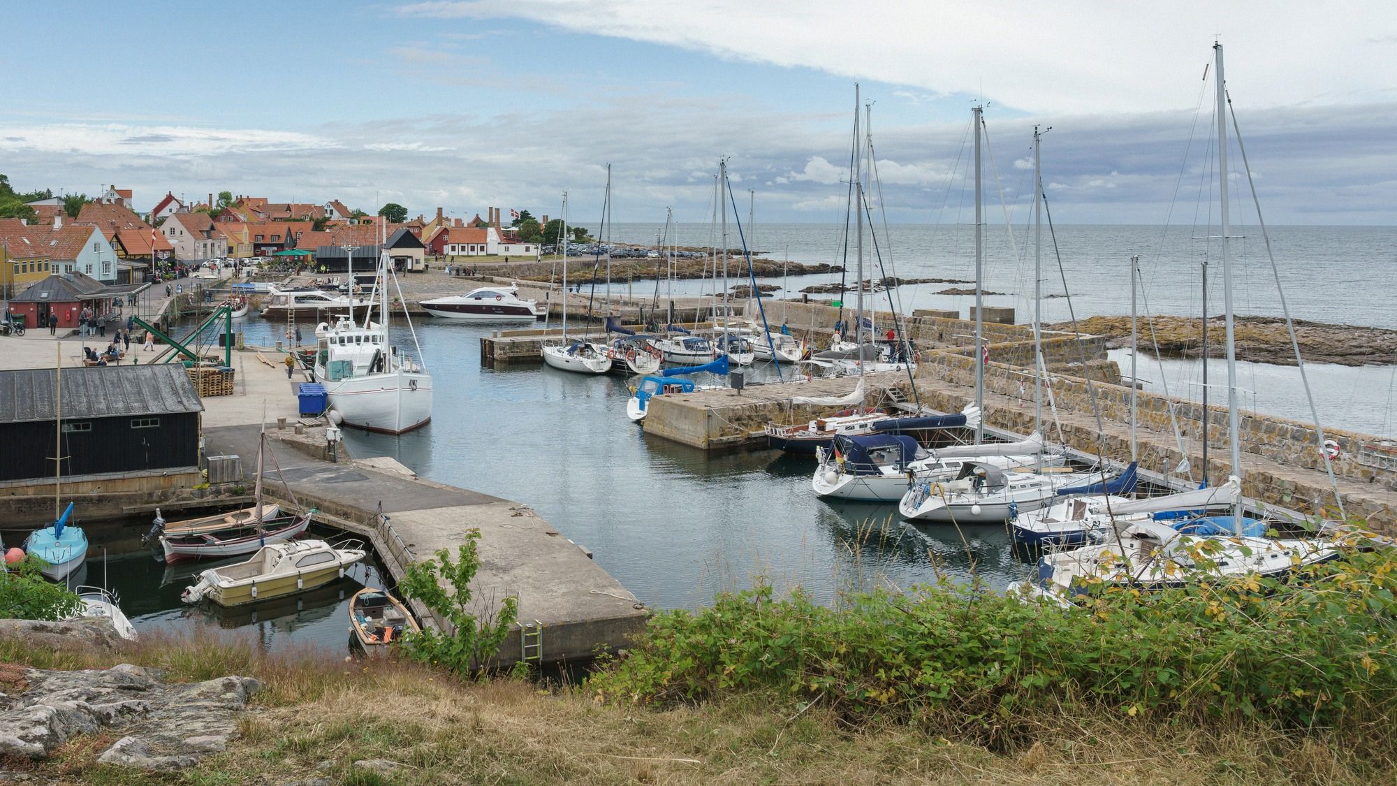 Weißes Räuche­reihaus mit charakteristischen Schornsteinen über dem Gudhjem-Hafen an Bornholms Ostküste.