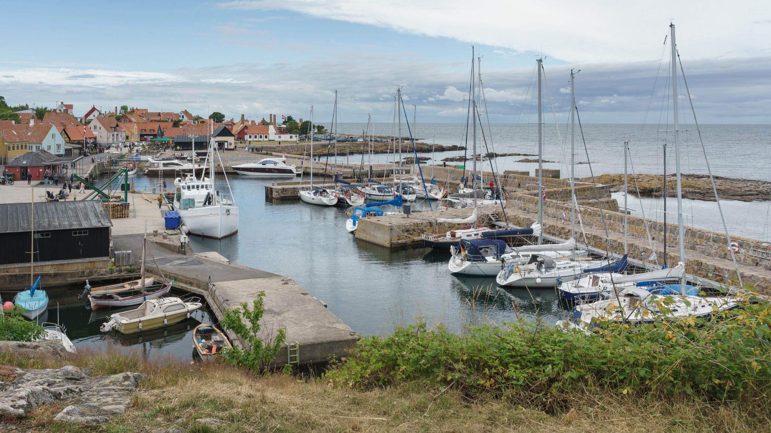Weißes Räuche­reihaus mit charakteristischen Schornsteinen über dem Gudhjem-Hafen an Bornholms Ostküste.