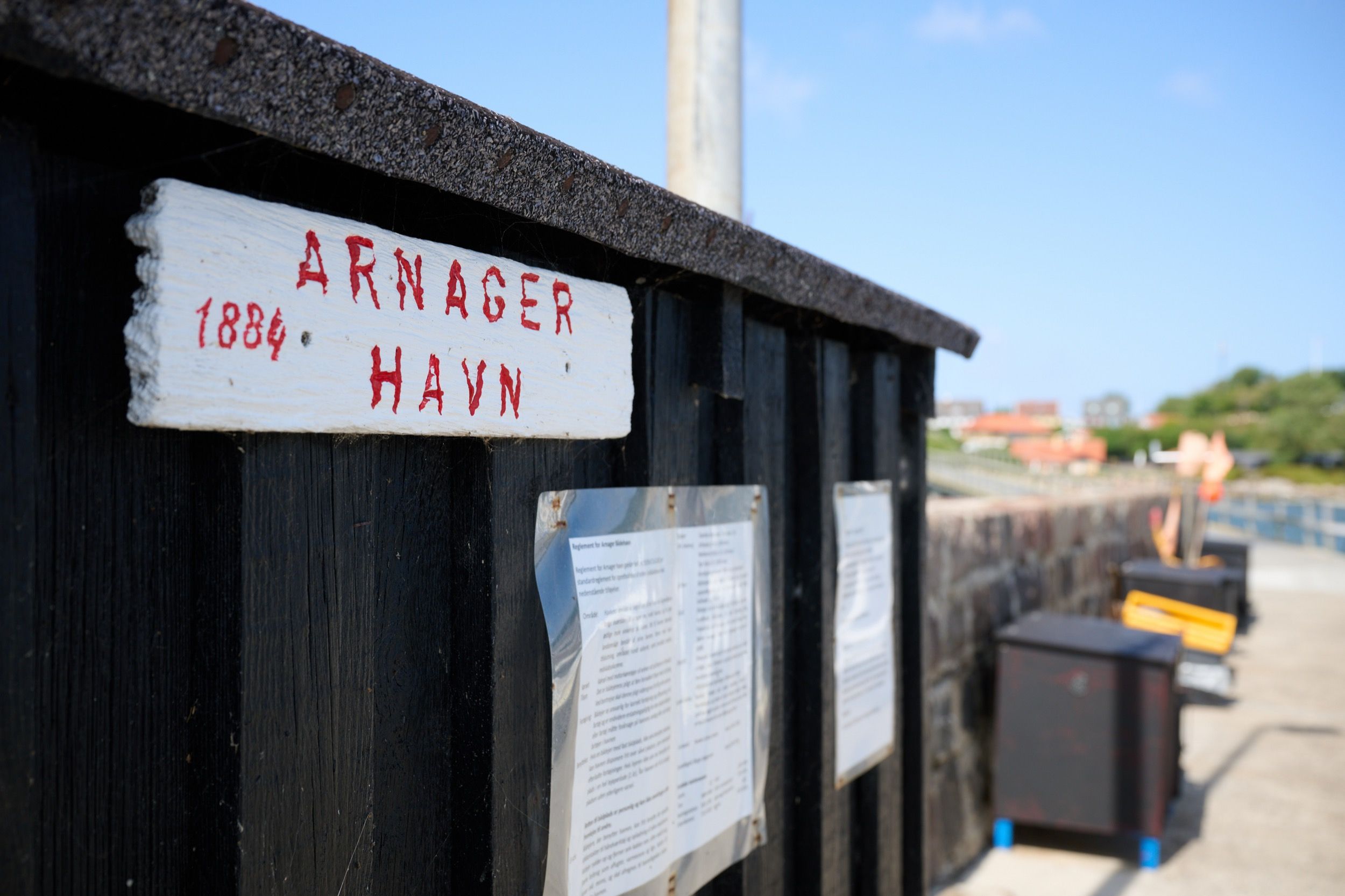 Nahaufnahme des handgemalten Ortsschilds 'Arnager Havn 1884' an einem schwarzen Holzhaus am kleinen Fischerhafen von Arnager.