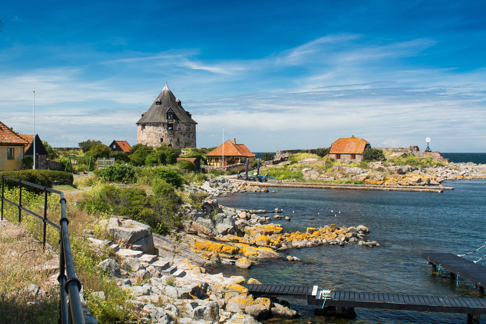 Defence tower and red roofs above the harbour bay of the pea islands. Rocky harbour of Christiansø with a round defence tower and red roofs