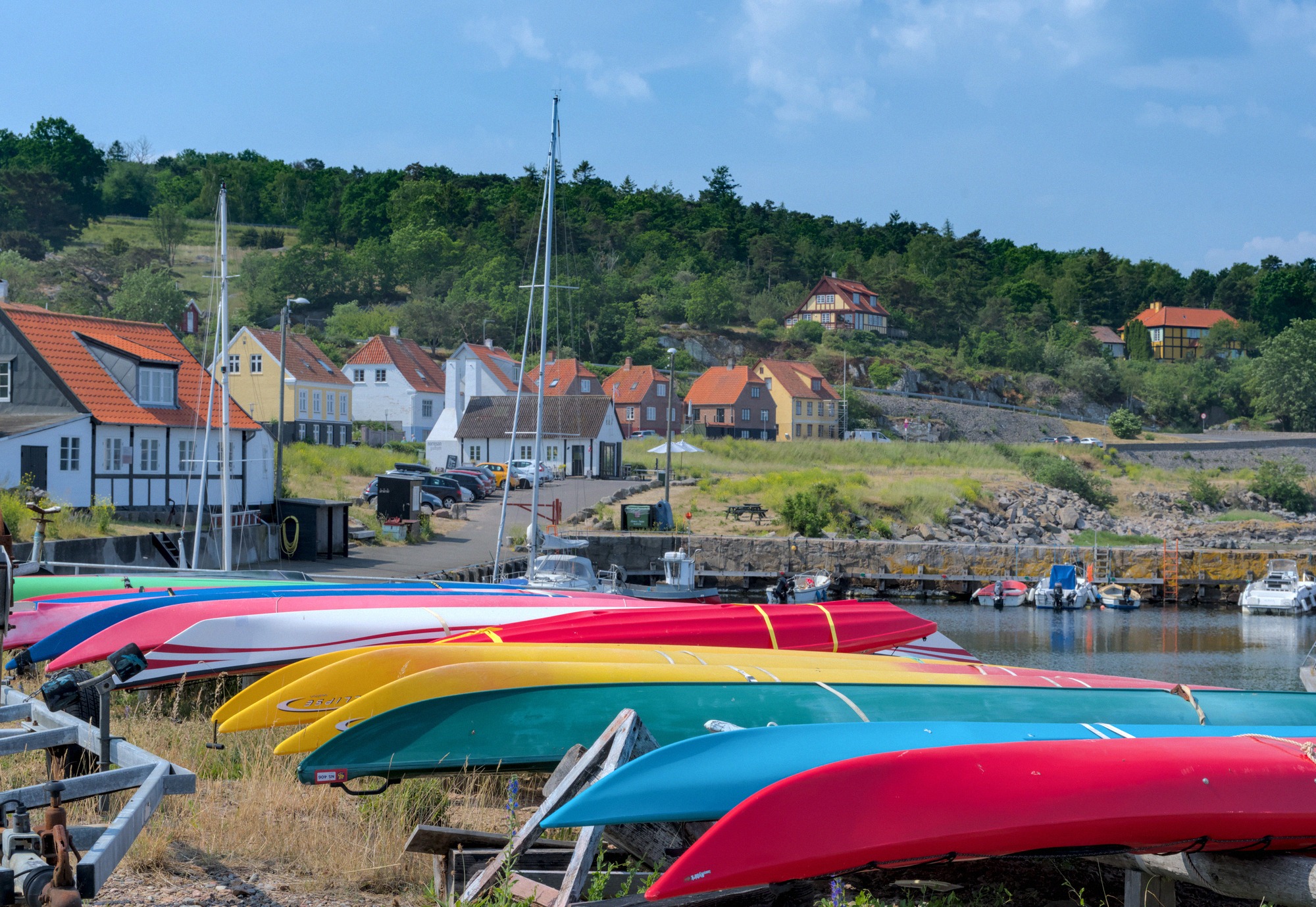 Gudhjem harbour, with the houses climbing the hillside behind. Colourful kayaks on the quay at Gudhjem harbour, with the houses climbing the hill behind