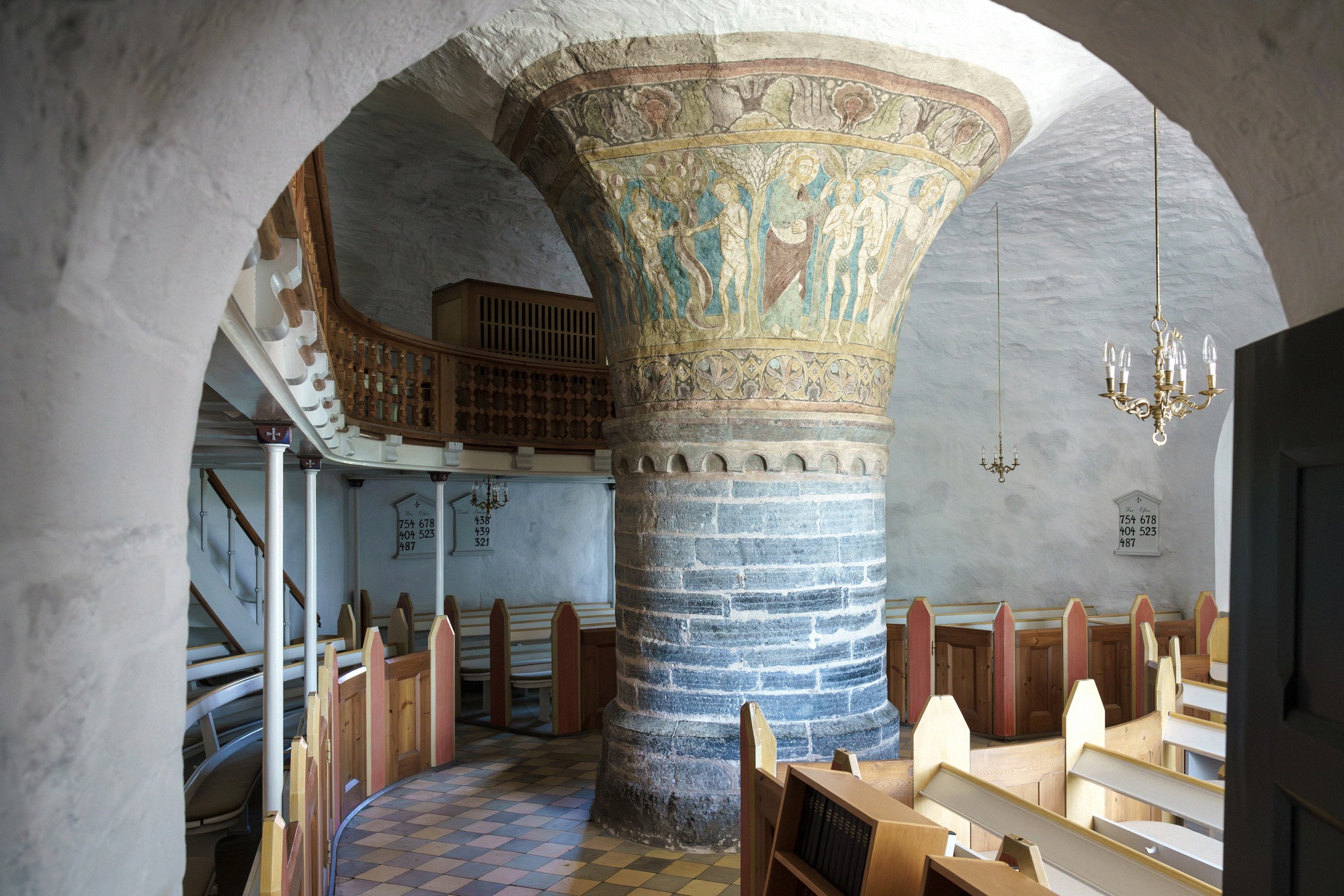 Interior of Nylars Church with the central pillar and colourful wooden pews