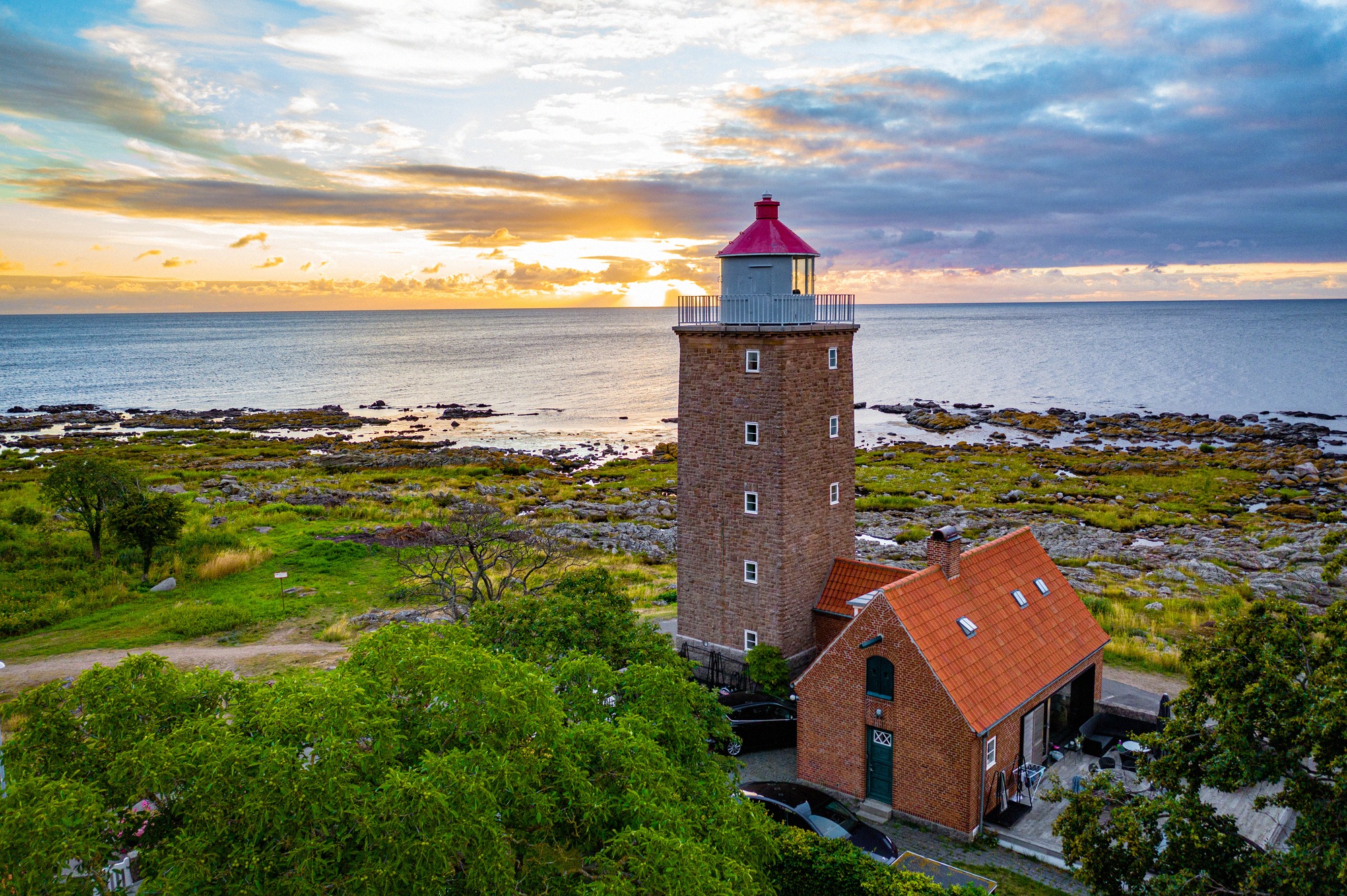 Aerial view of the red-roofed brick lighthouse Svaneke Fyr on the rocky coast