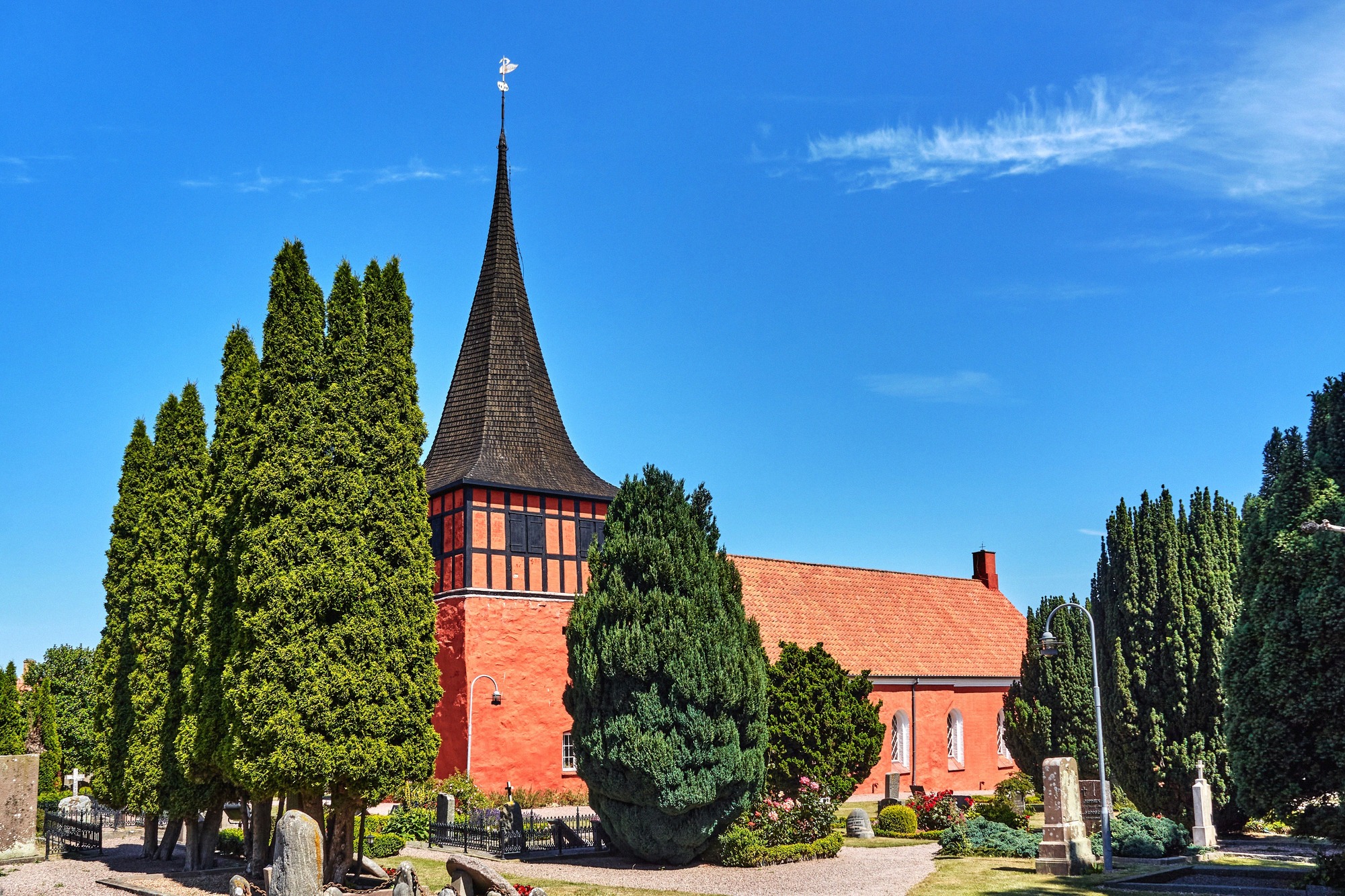 The red-brick church of Svaneke with its black timber-clad tower among cypress trees