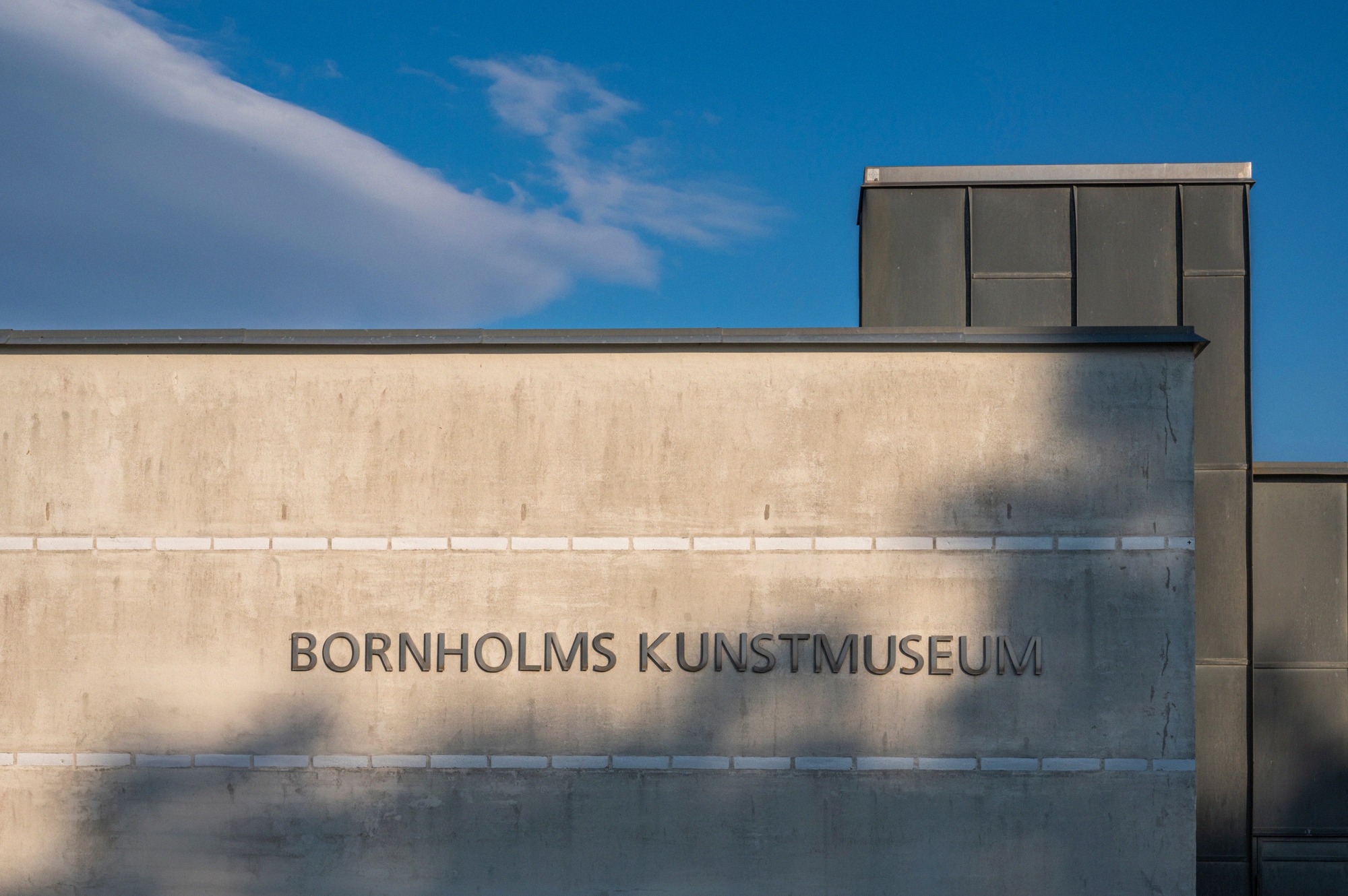 Aussenfassade des Bornholms Kunstmuseum in Gudhjem mit dem eingravierten Schriftzug im Betonbau unter blauem Himmel.